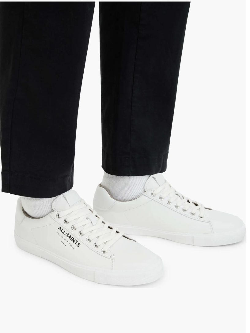 Man wearing white AllSaints Underground leather low-top sneakers with black trousers and white socks.