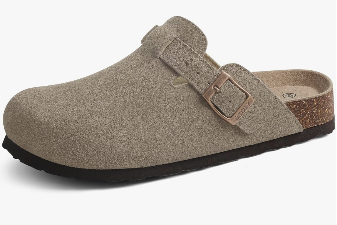 A pair of taupe suede men's mules featuring a backless design, an adjustable buckle strap, and a contoured cork footbed for a modern 2026 summer look.
