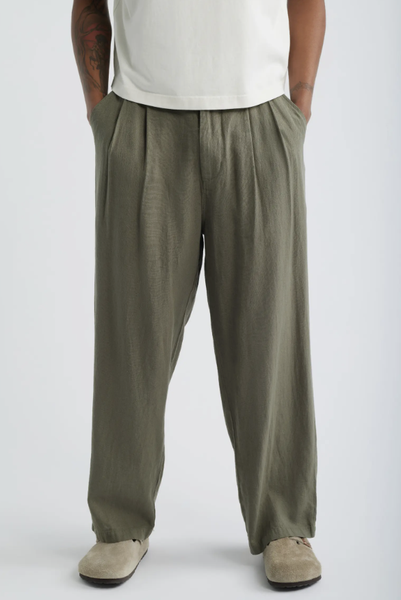 A man wearing straight-leg olive green linen trousers paired with beige suede shoes, styled for a relaxed 2026 summer look.