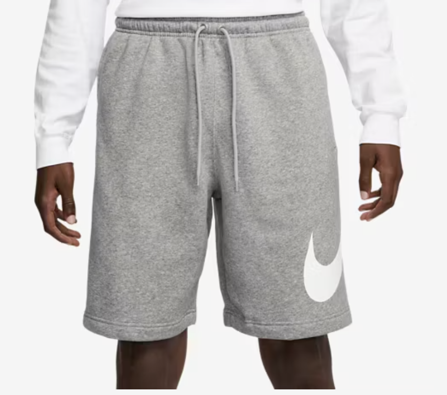 A man wearing grey Nike Solo Swoosh fleece shorts with a white embroidered swoosh logo, styled for a premium minimalist streetwear look.