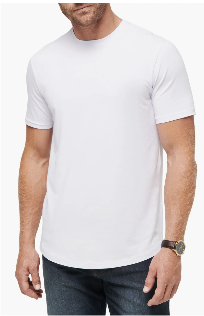 Man wearing a white TravisMathew Cloud Crewneck T-shirt tucked into dark wash denim jeans.