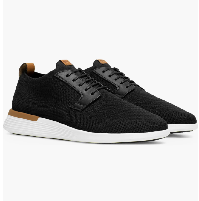 A pair of black Wolf & Shepherd Swiftknit Derby sneakers featuring a breathable knit upper, leather accents on the heel and tongue, and a clean white athletic sole for a 2026 hybrid dress-casual look.