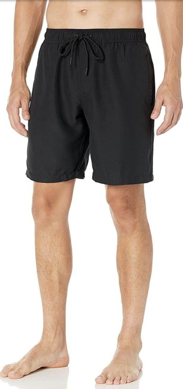 A close-up view of a person wearing classic black Amazon Essentials quick-dry swim trunks, showcasing the clean fit, standard length, and comfortable elastic drawstring waistband.