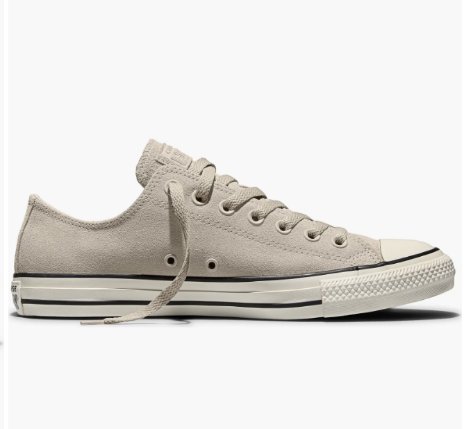 A side profile shot of a classic white canvas Converse Chuck Taylor All Star low-top sneaker with its signature white rubber toe cap and red and blue foxing stripes.