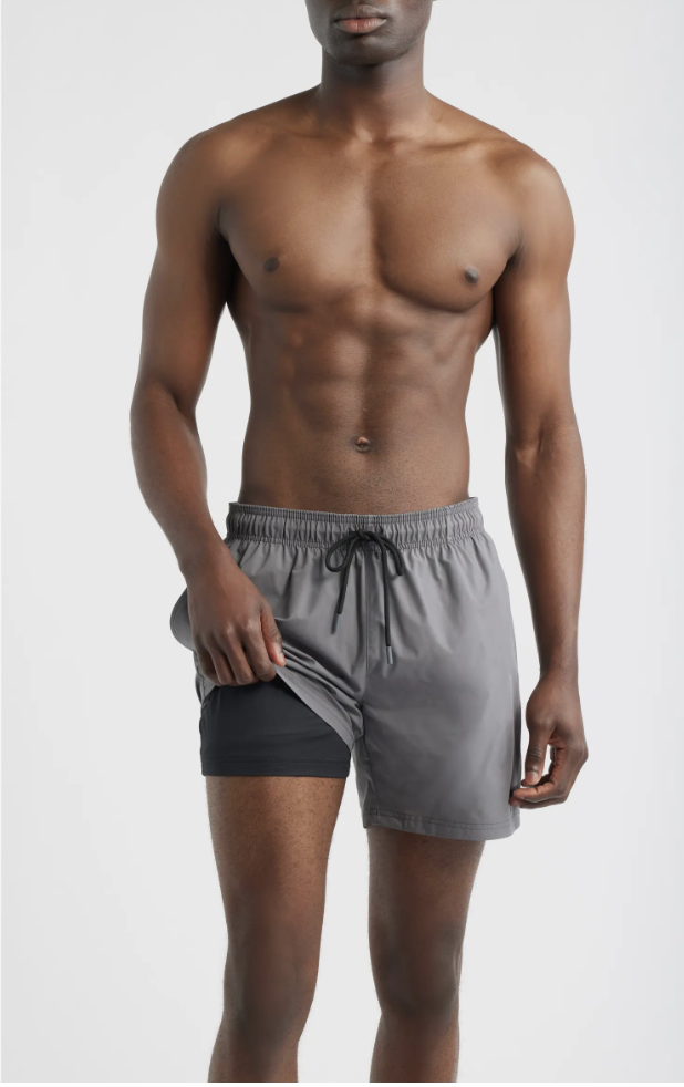 A close-up, mid-torso view of a model wearing dark grey Boss swim trunks featuring a classic drawstring waistband and a subtle built-in mesh boxer-brief liner visible at the thigh.