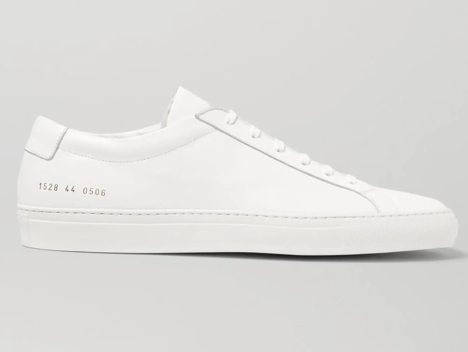 A side profile view of a luxury white leather Common Projects Original Achilles Low sneaker, showcasing its minimal design and signature gold serial number stamped on the heel.