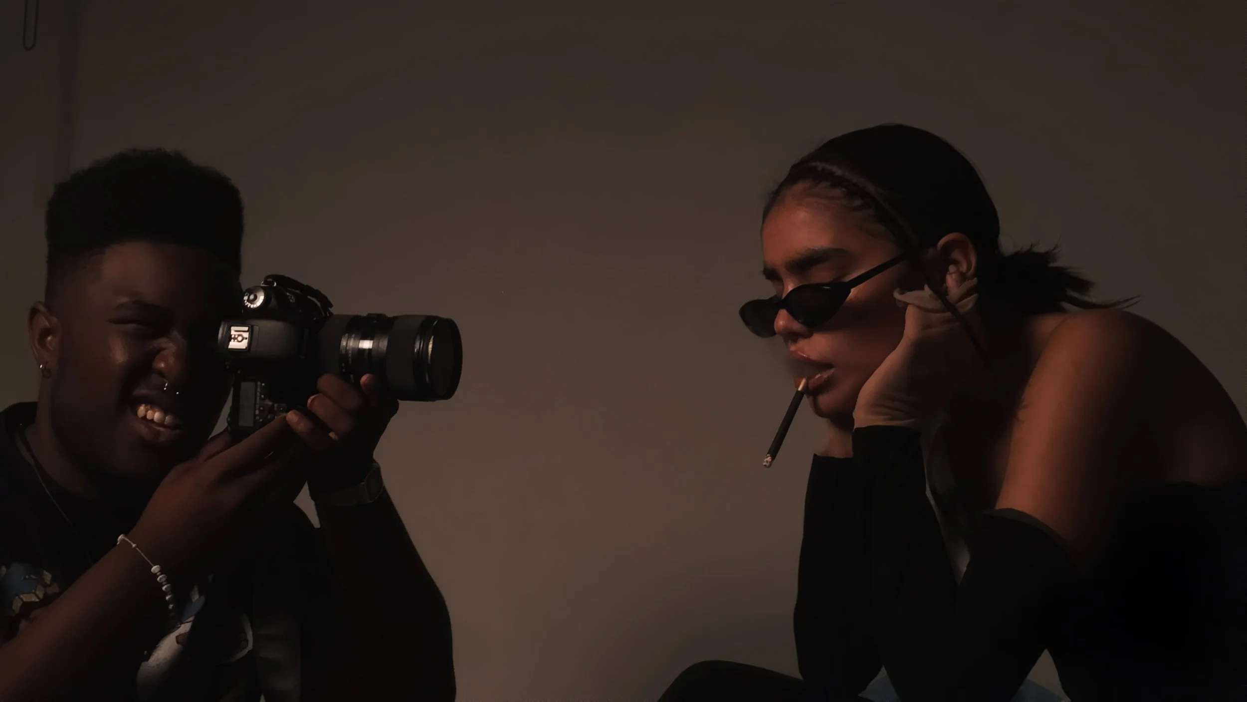 Two people, one with a camera and one with a cigarette, in a dark room.