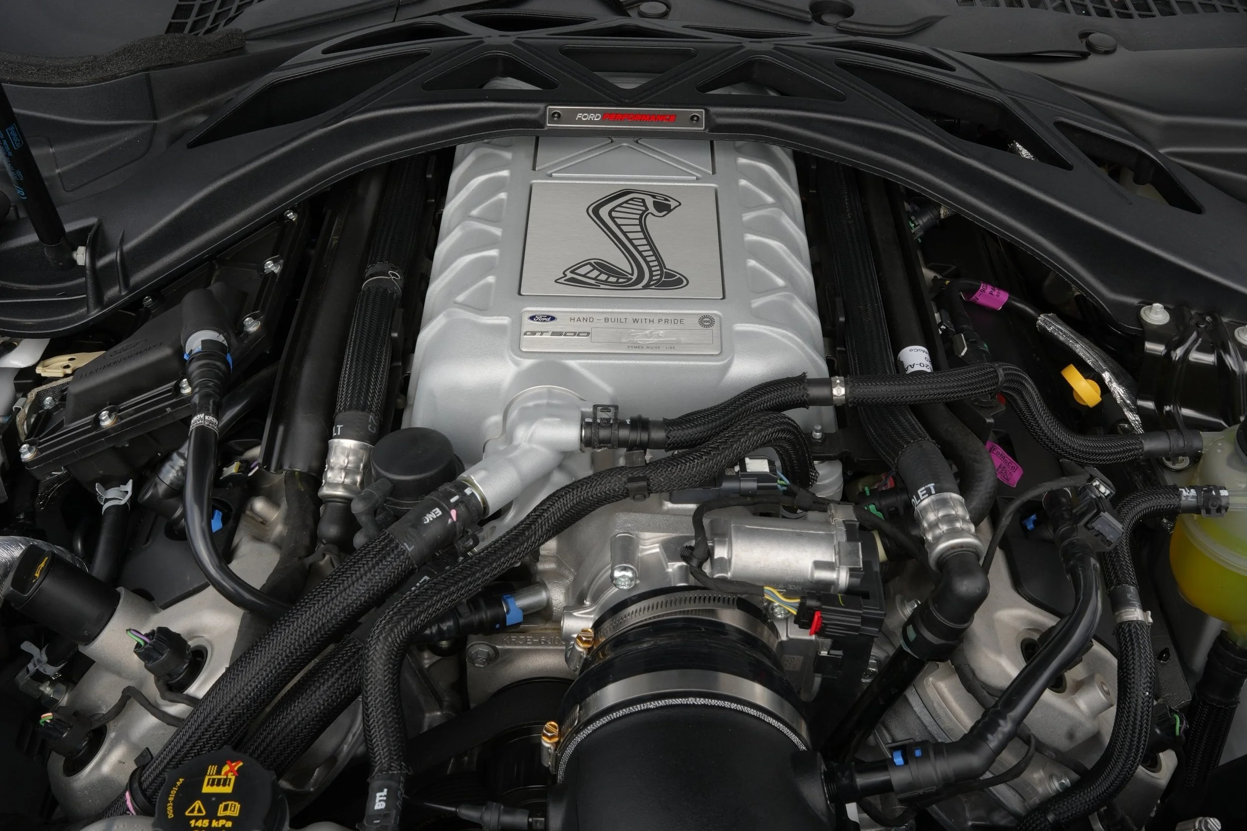 Close-up view of a Ford Mustang Shelby GT500 engine bay, showcasing the supercharged V8 engine with Cobra logo on the intake cover.