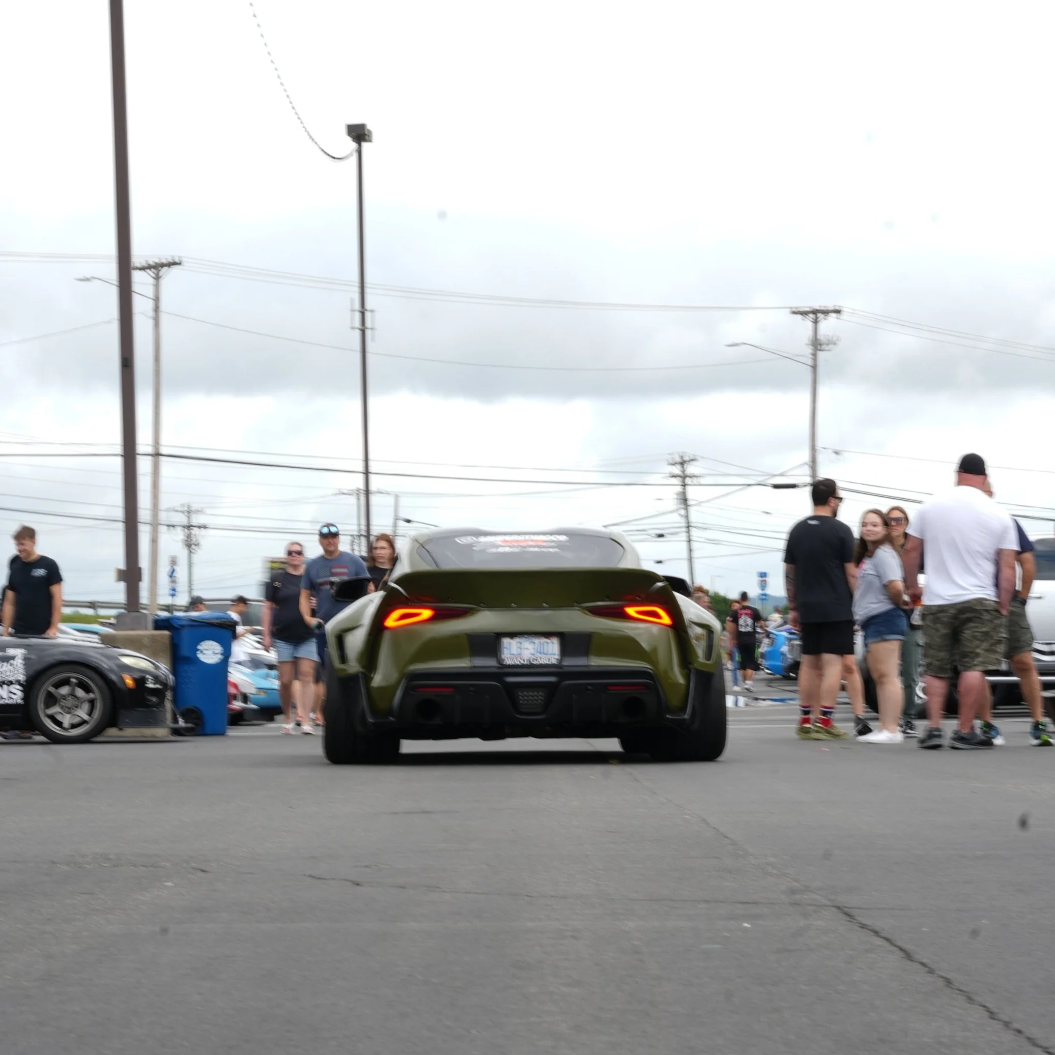 Green sports car at a car meet with people standing around and other cars parked nearby.