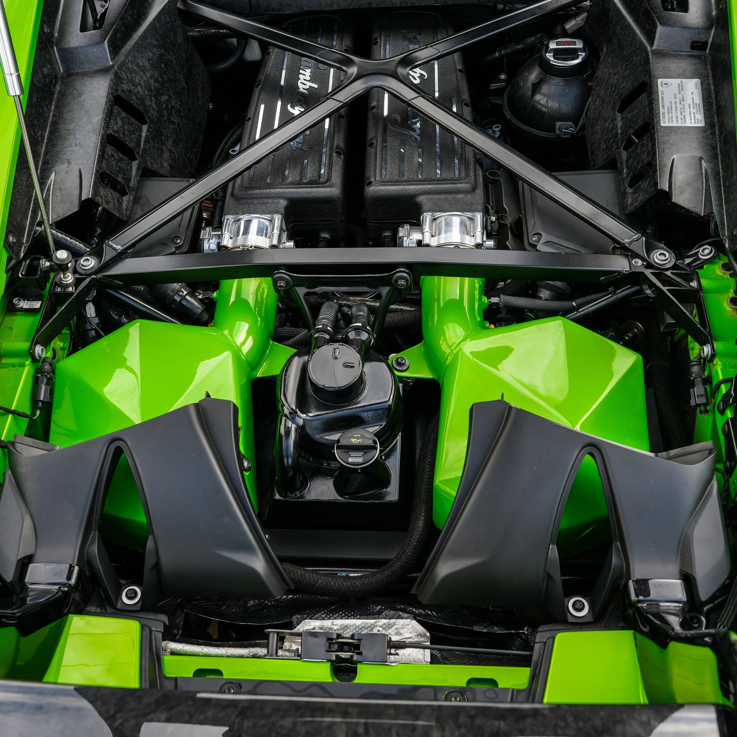 Close-up of the engine bay of a bright green sports car, showing the engine, black and silver components, and surrounding parts.
