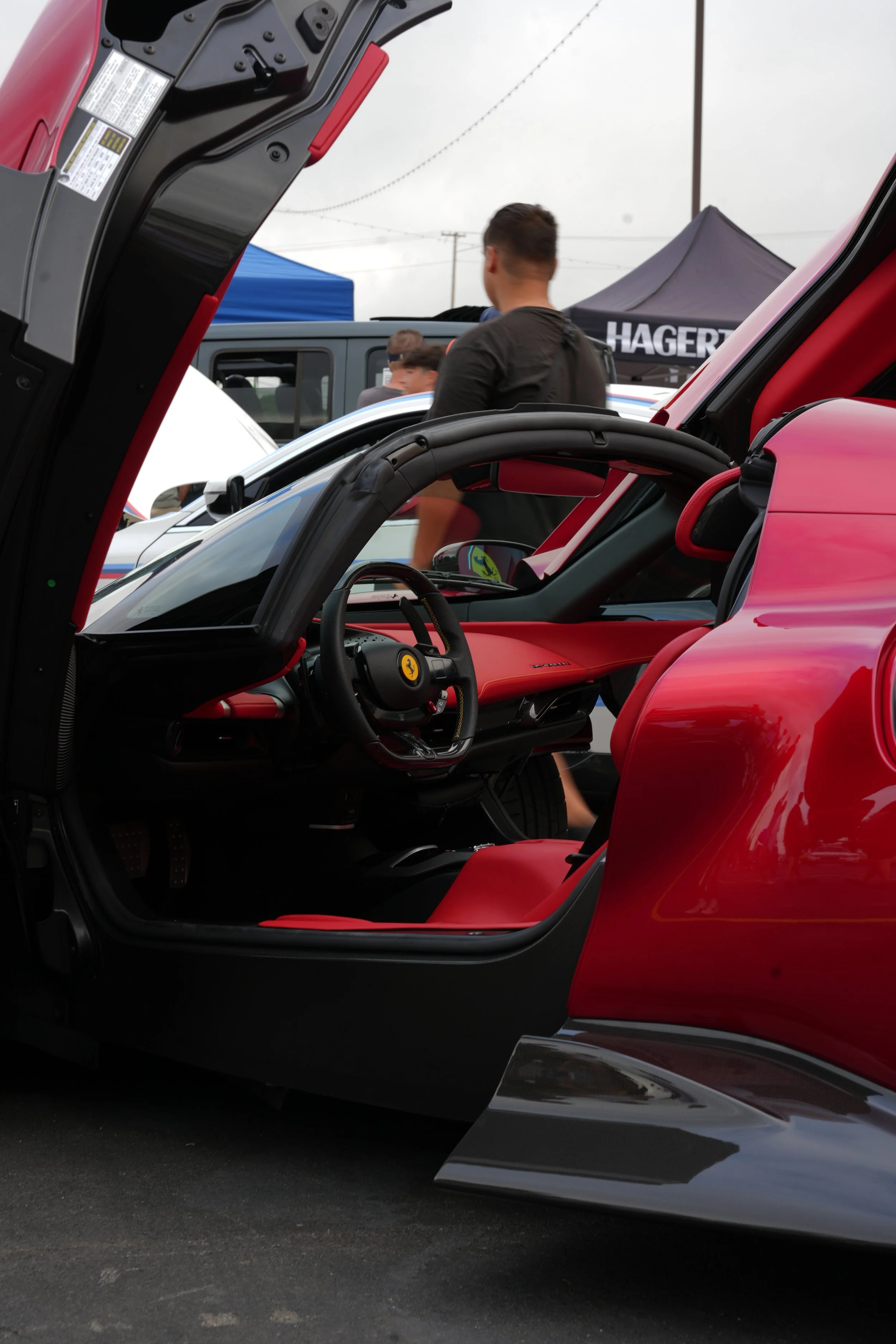 Close-up of the interior of a red Ferrari sports car with the driver's door open, showing the black steering wheel with the Ferrari logo and red interior seats, at a car show.