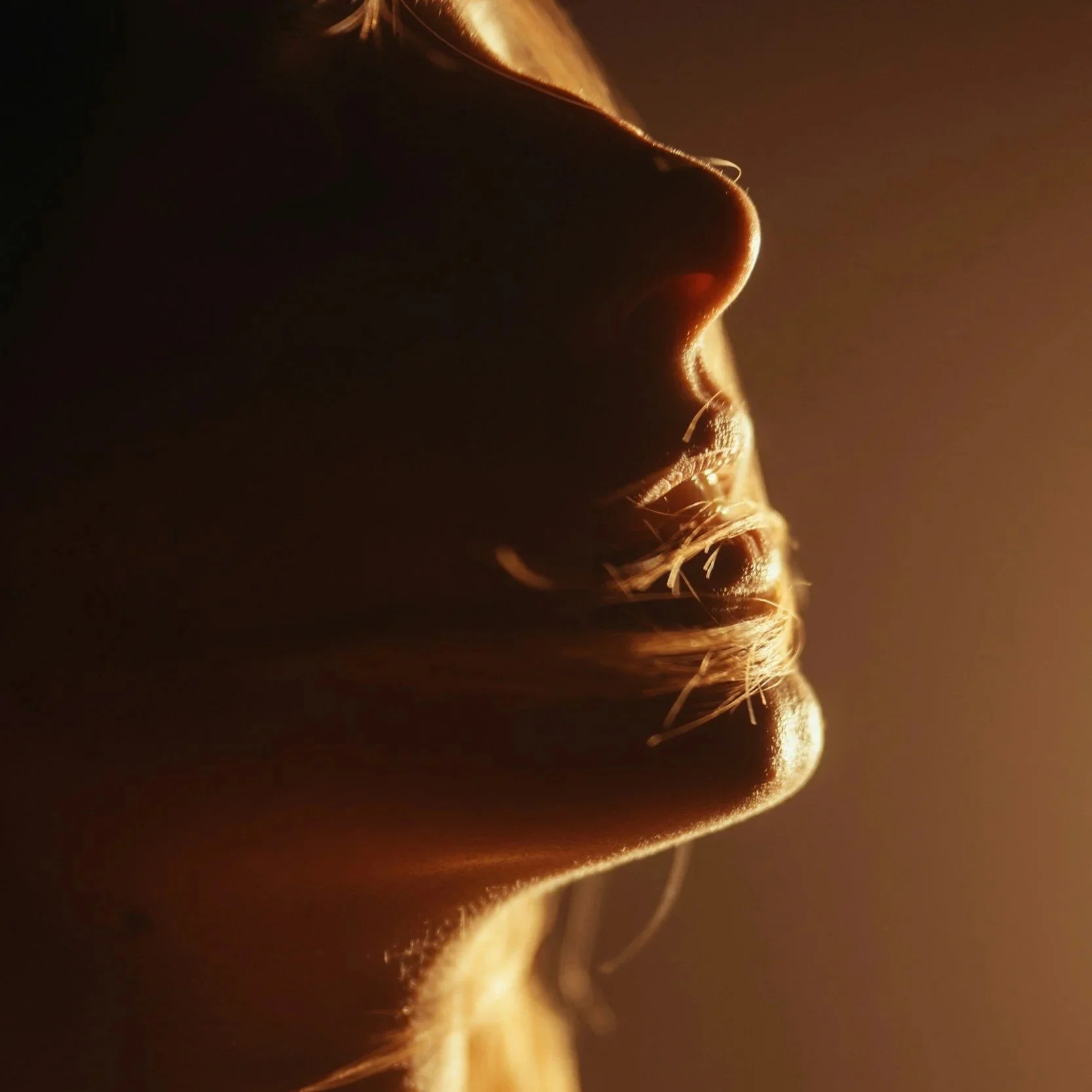 Close-up of a person's face in profile with warm backlighting accentuating facial features and skin texture.