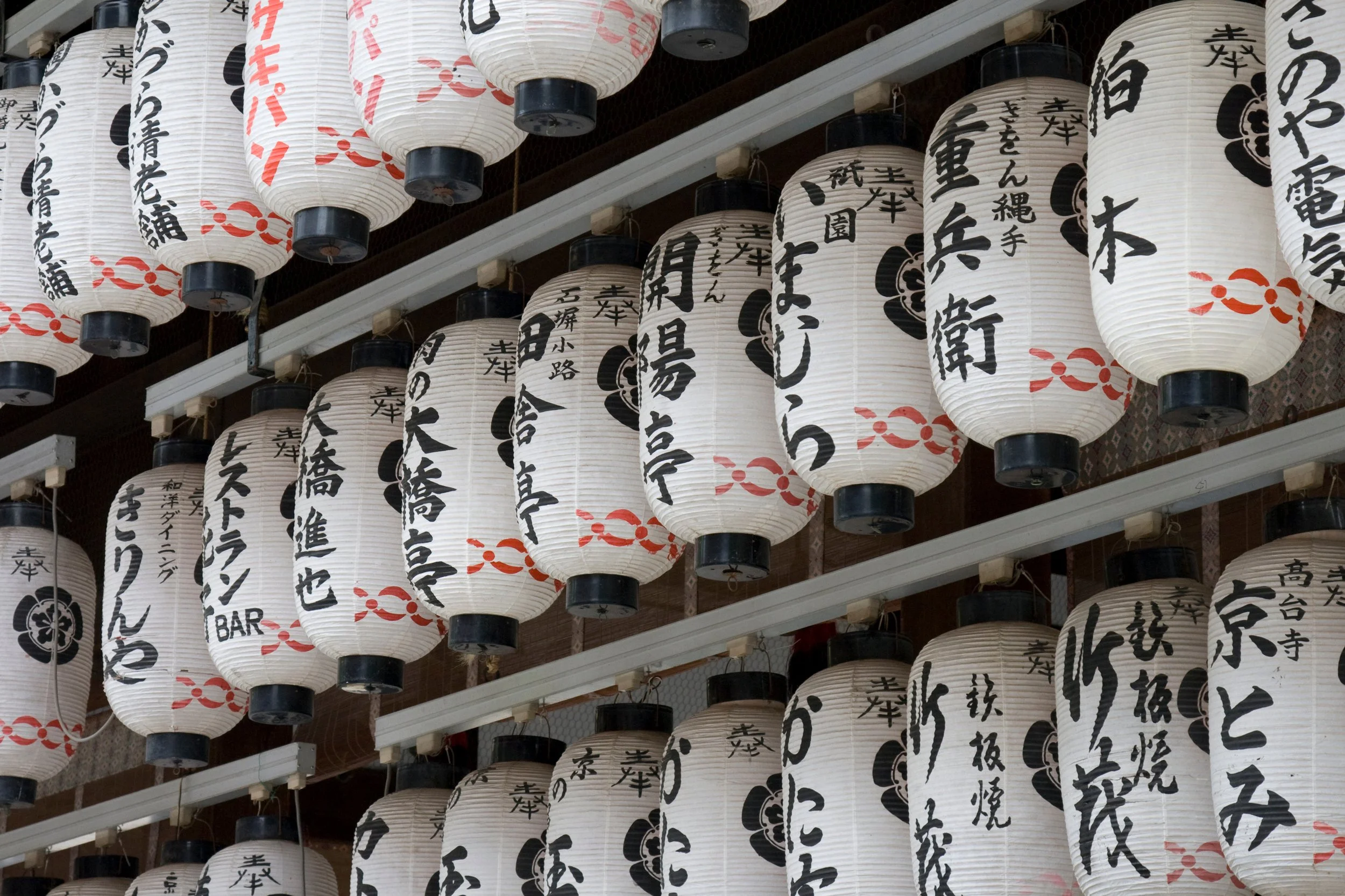 Japanese paper lanterns with black and red kanji characters hanging in a row at a festival or shrine.