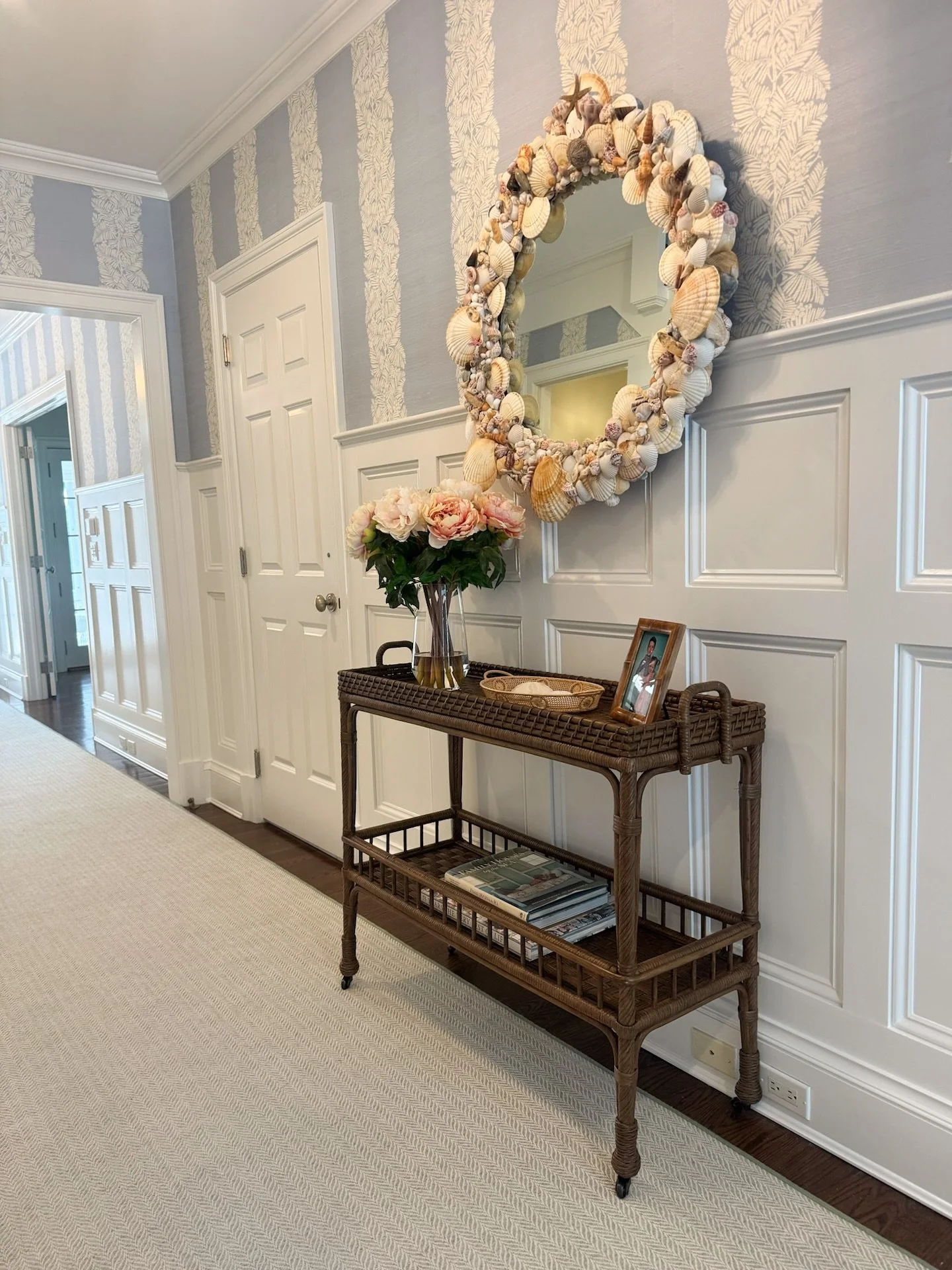 A warm welcome with a seaside twist: this Southampton entryway sets the tone with coastal-inspired details: an incredible shell mirror from @1stdibs + a @brunschwigfils nature-inspired wallpaper, and a @serenaandlily bar cart that&rsquo;s equal parts