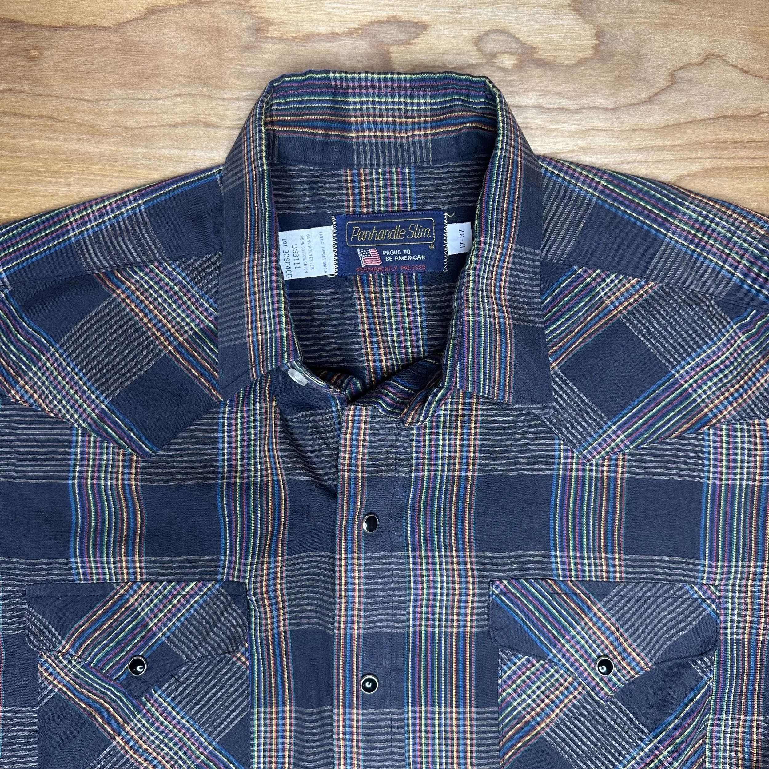 Close-up of vintage Panhandle Slim rainbow-striped plaid pearl snap shirt, showcasing collar, label, and vibrant colors.