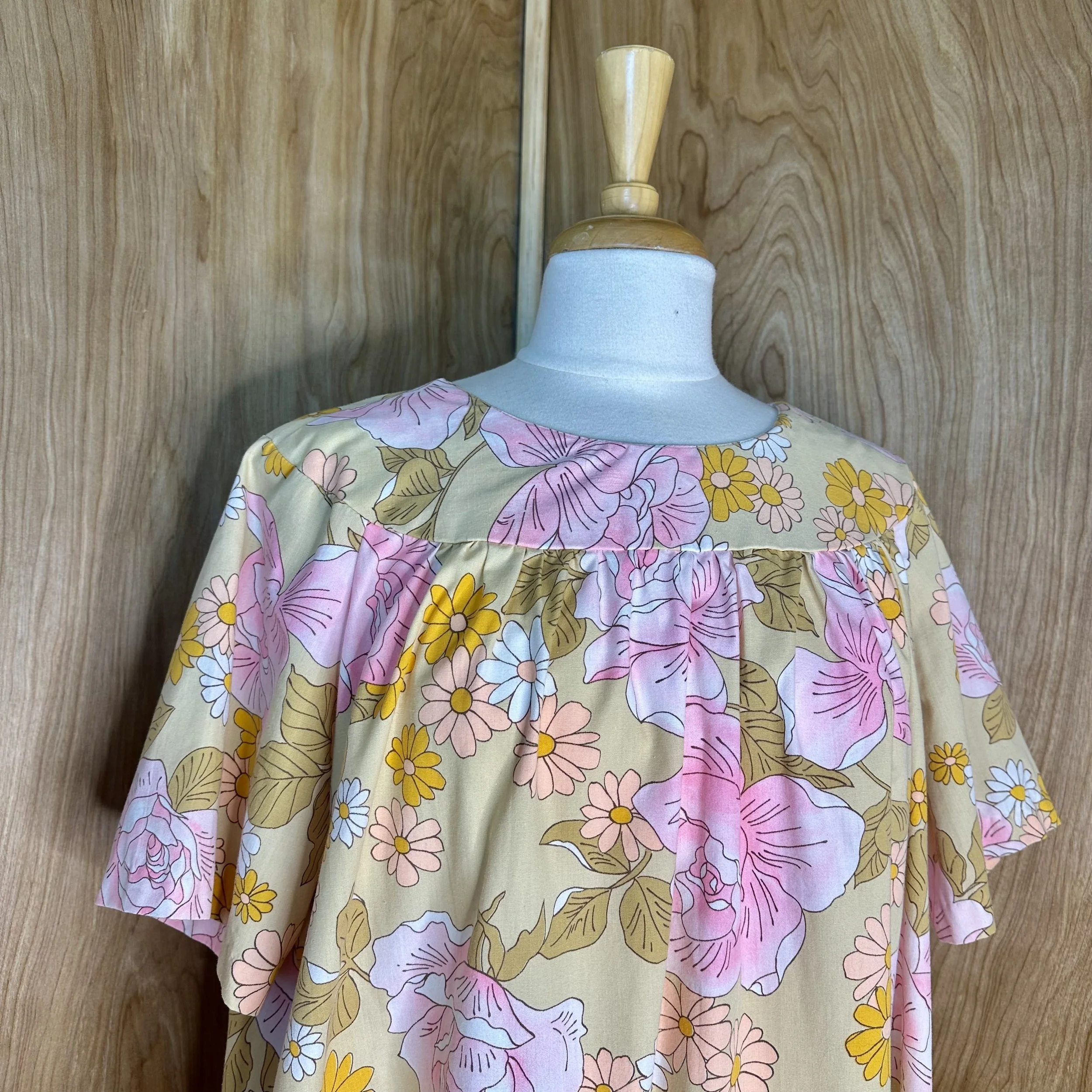 Vintage 70s muumuu dress on mannequin, relaxed fit with colorful floral pattern, side view.