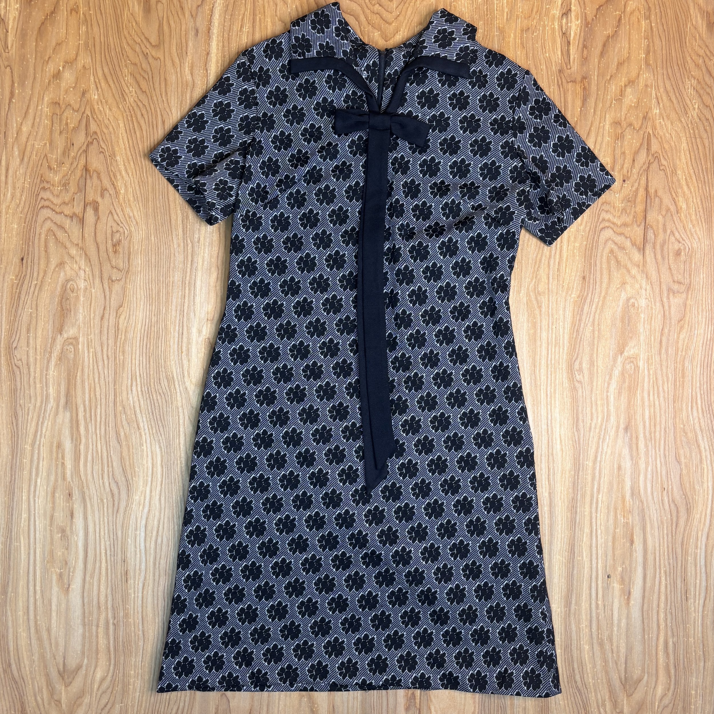 Full front view of the 1960s Westover mod dress with black floral knit and bow collar, laid flat on wooden background.