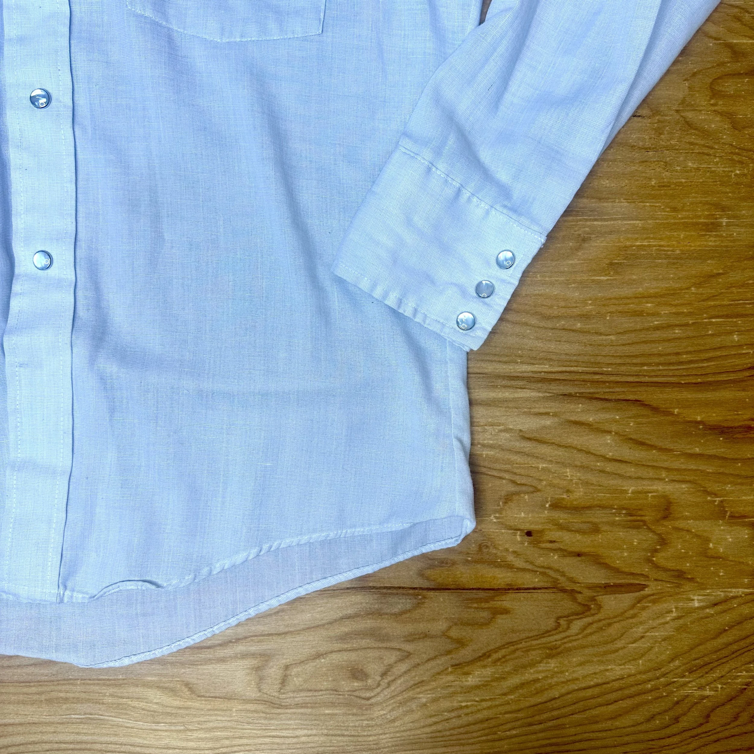 Close-up of hem and sleeve cuff with pearl snap buttons on light gray vintage western shirt.
