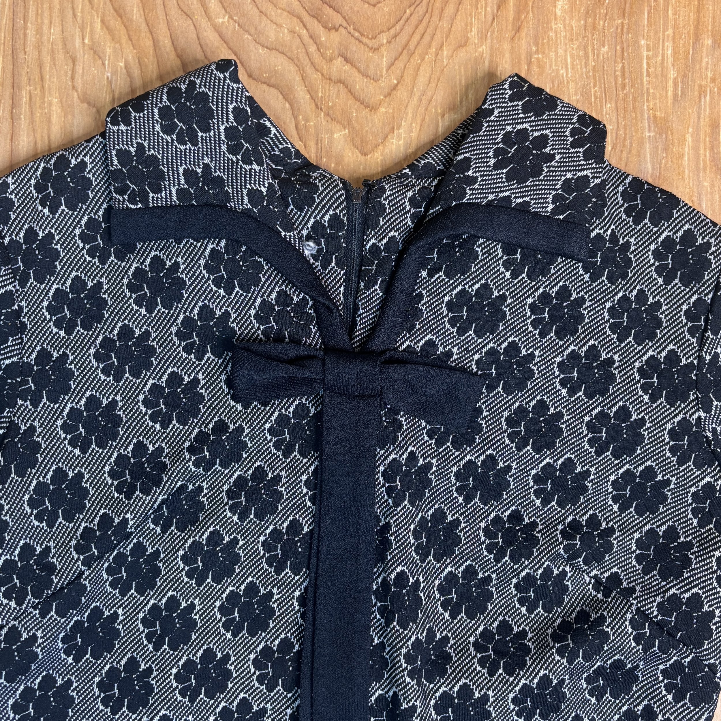 Detail shot of the collar and bow at the neckline, showing piping and texture.