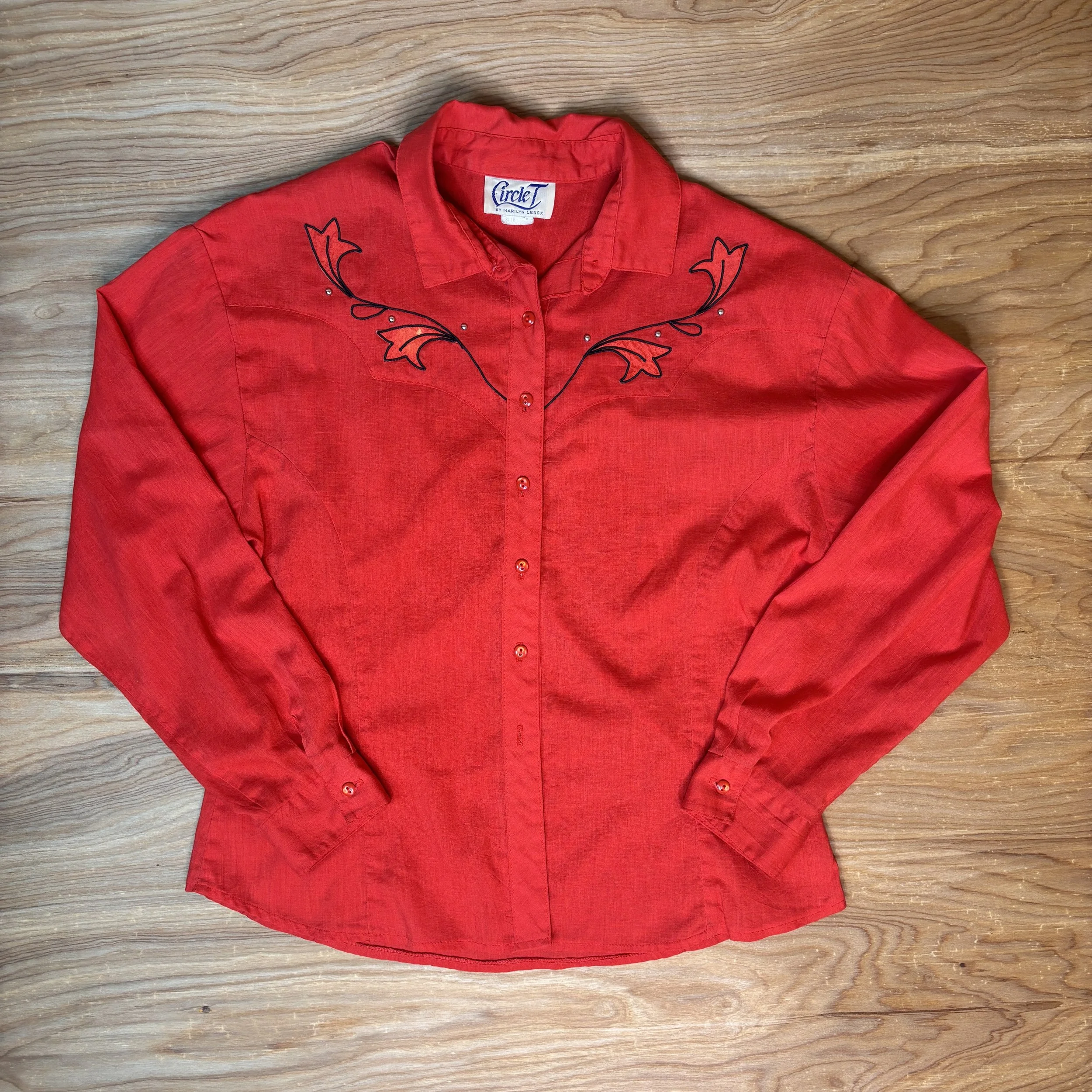 Front view of red embroidered Circle T western shirt laid flat on wood background