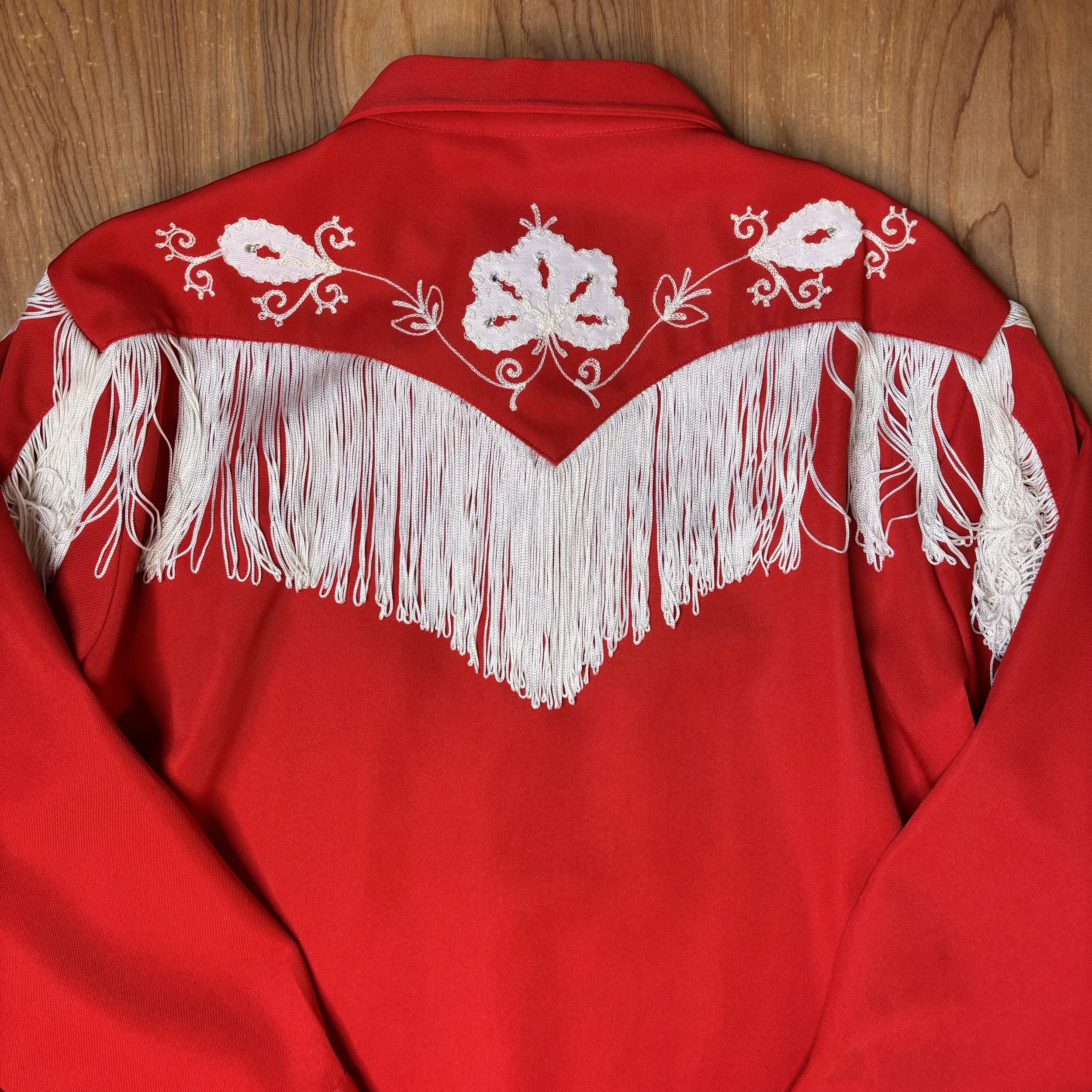 Back view of red western shirt with white floral embroidery and full yoke fringe