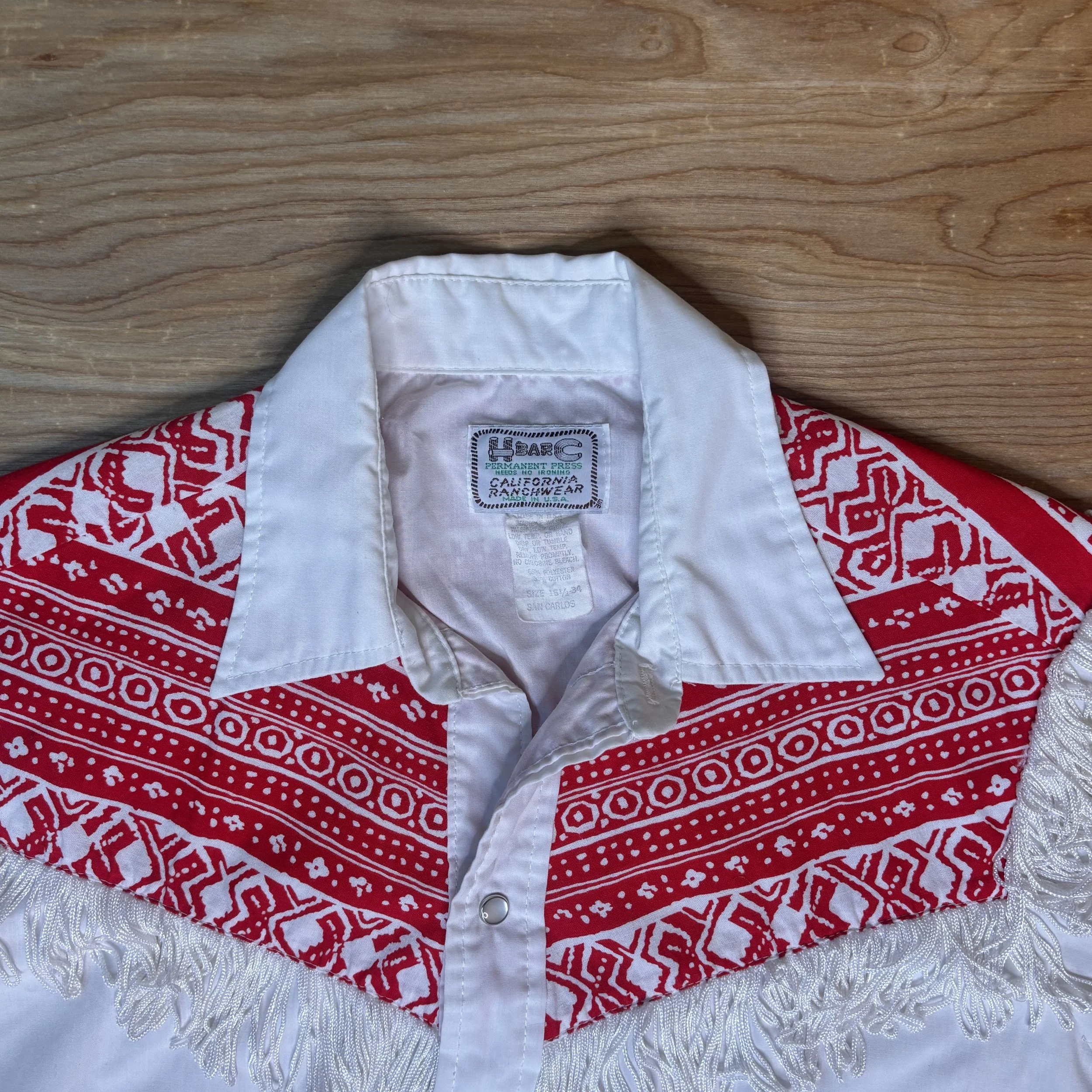 Close-up of H Bar C California Ranchwear label and pointed collar on red and white western shirt.