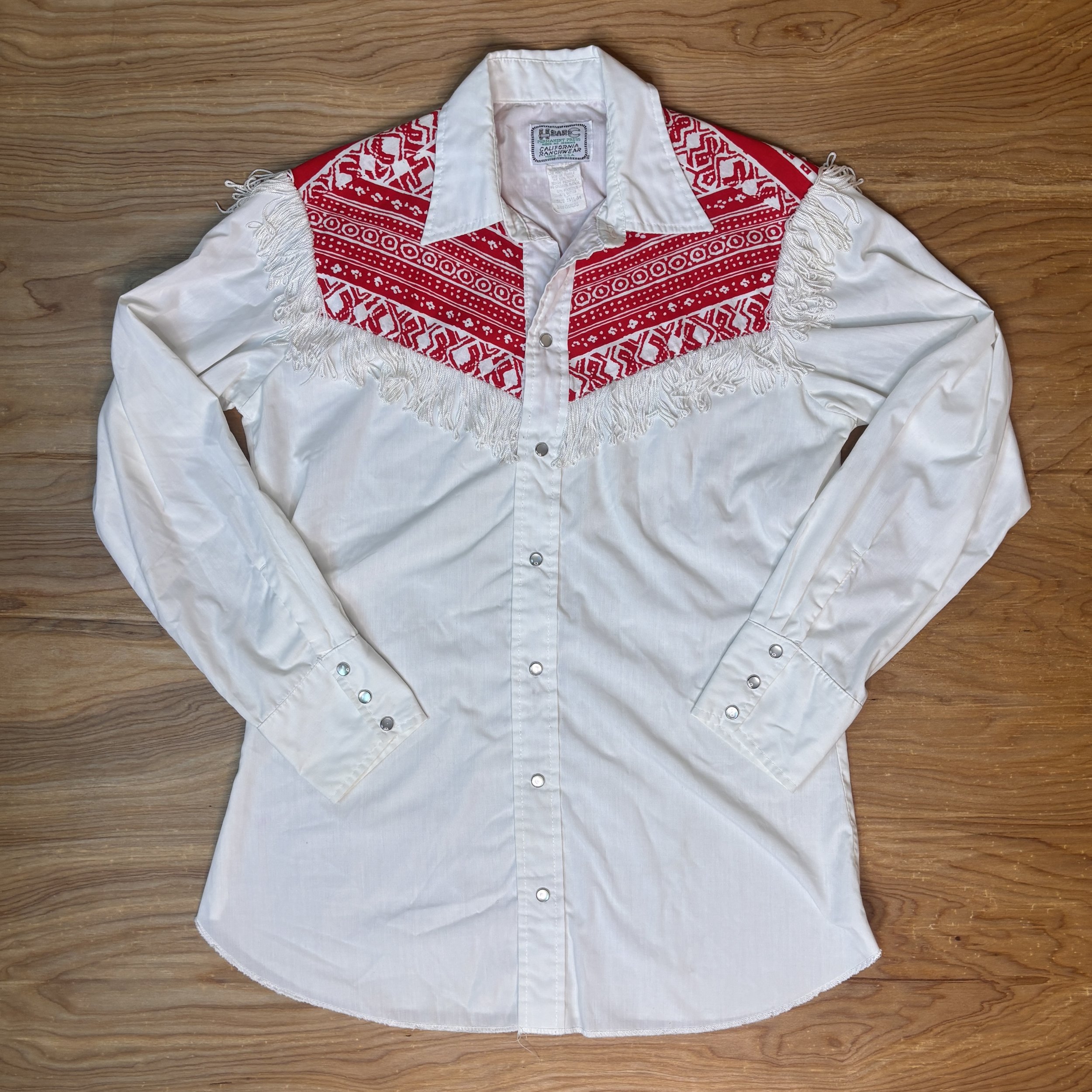 Vintage H Bar C women’s western shirt with red bandana yoke and white fringe, laid flat on wooden floor.