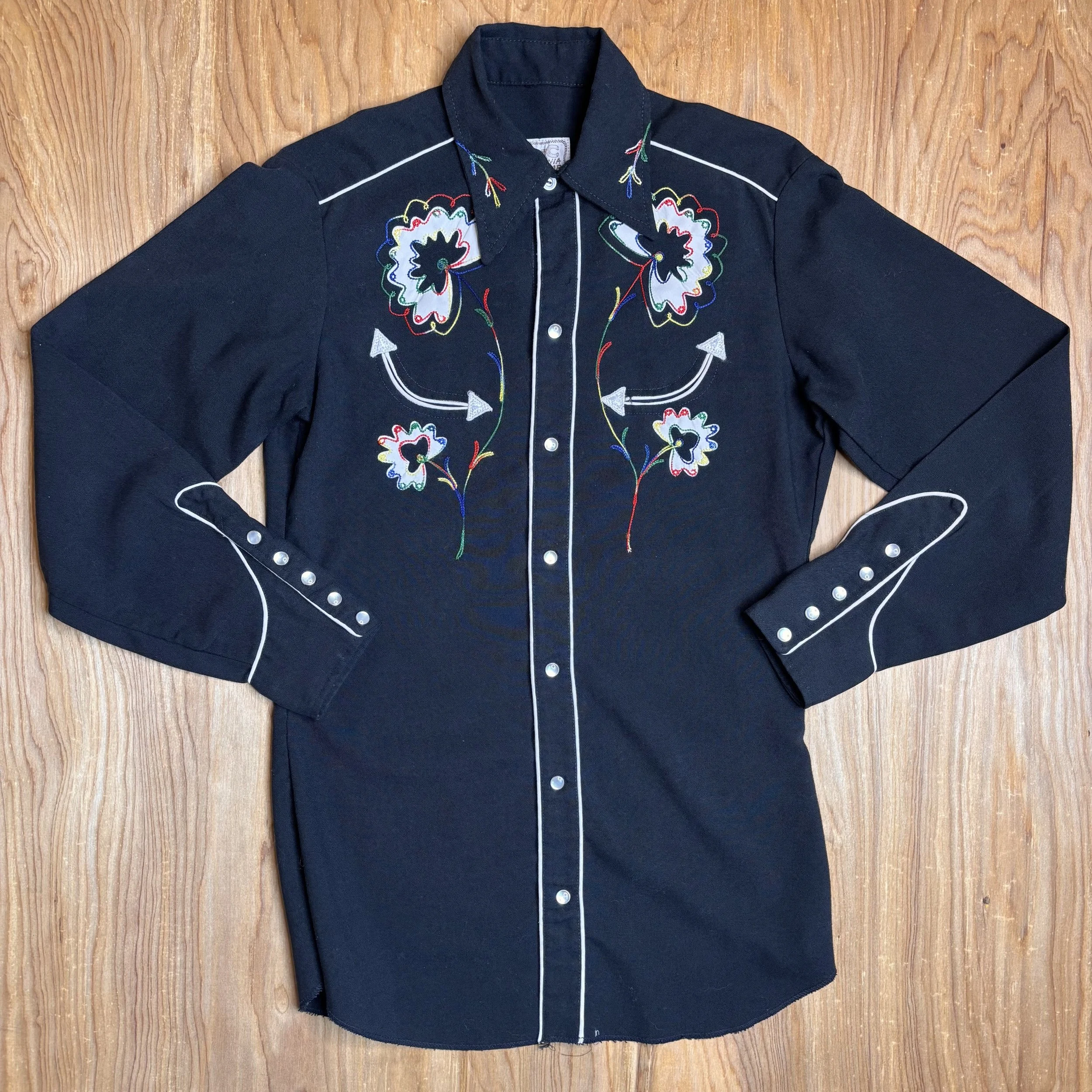 Front view of vintage black H Bar C pearl snap shirt with rainbow floral embroidery and white piping.