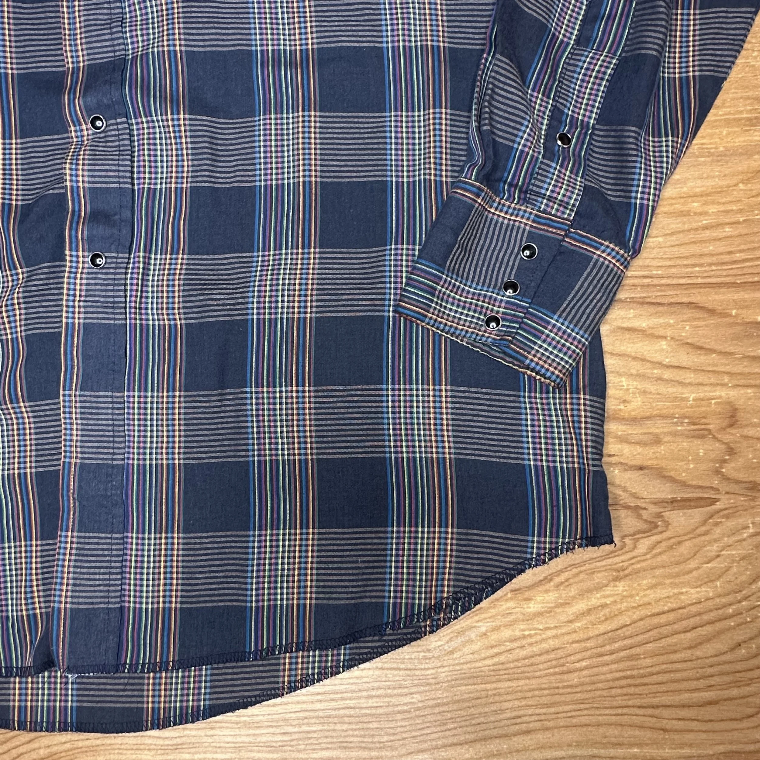 Close up view of vintage Western-style shirt, highlighting rainbow plaid pattern, pearl snaps, and pointed yokes.