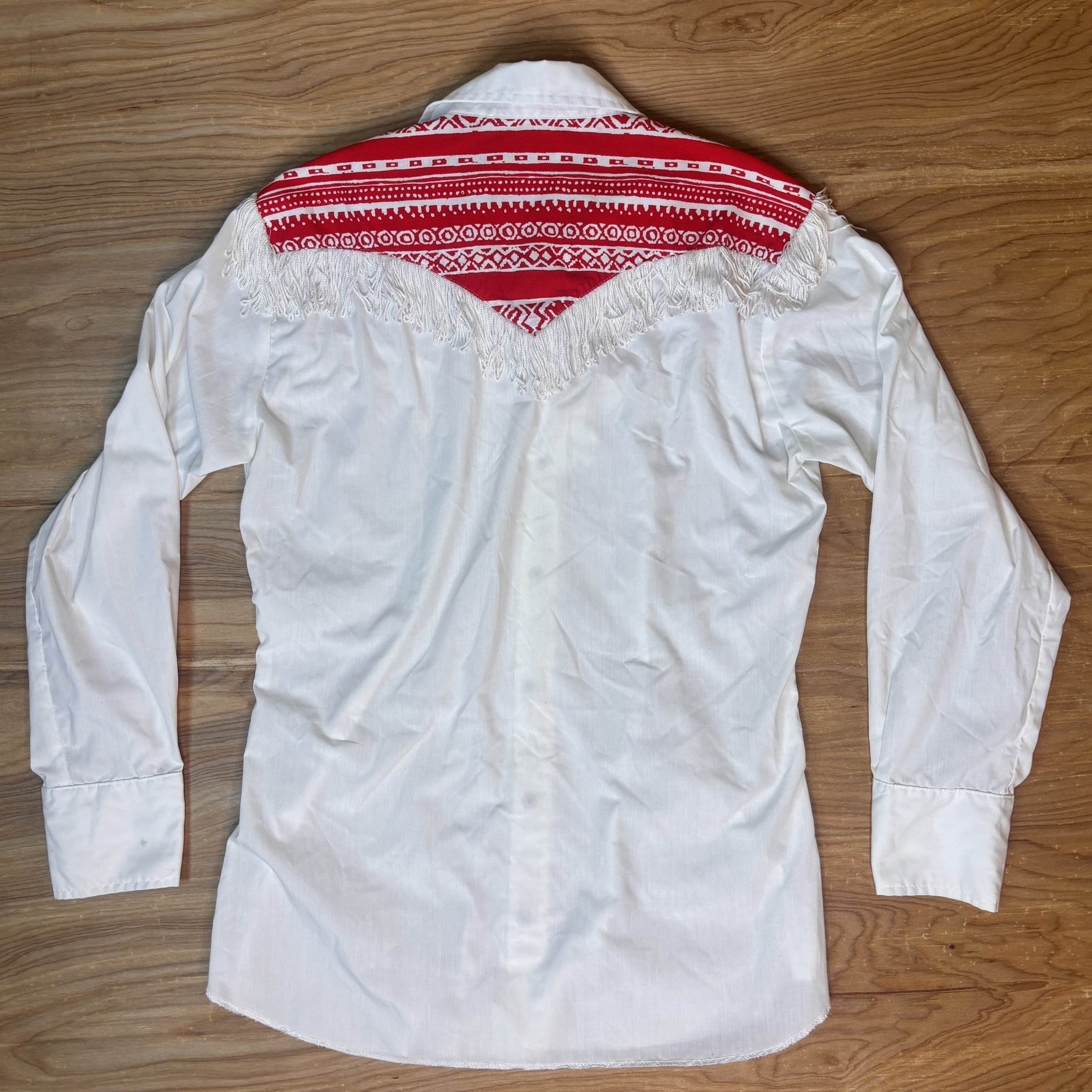 Back of vintage white western shirt with red patterned yoke and full fringe across shoulders.