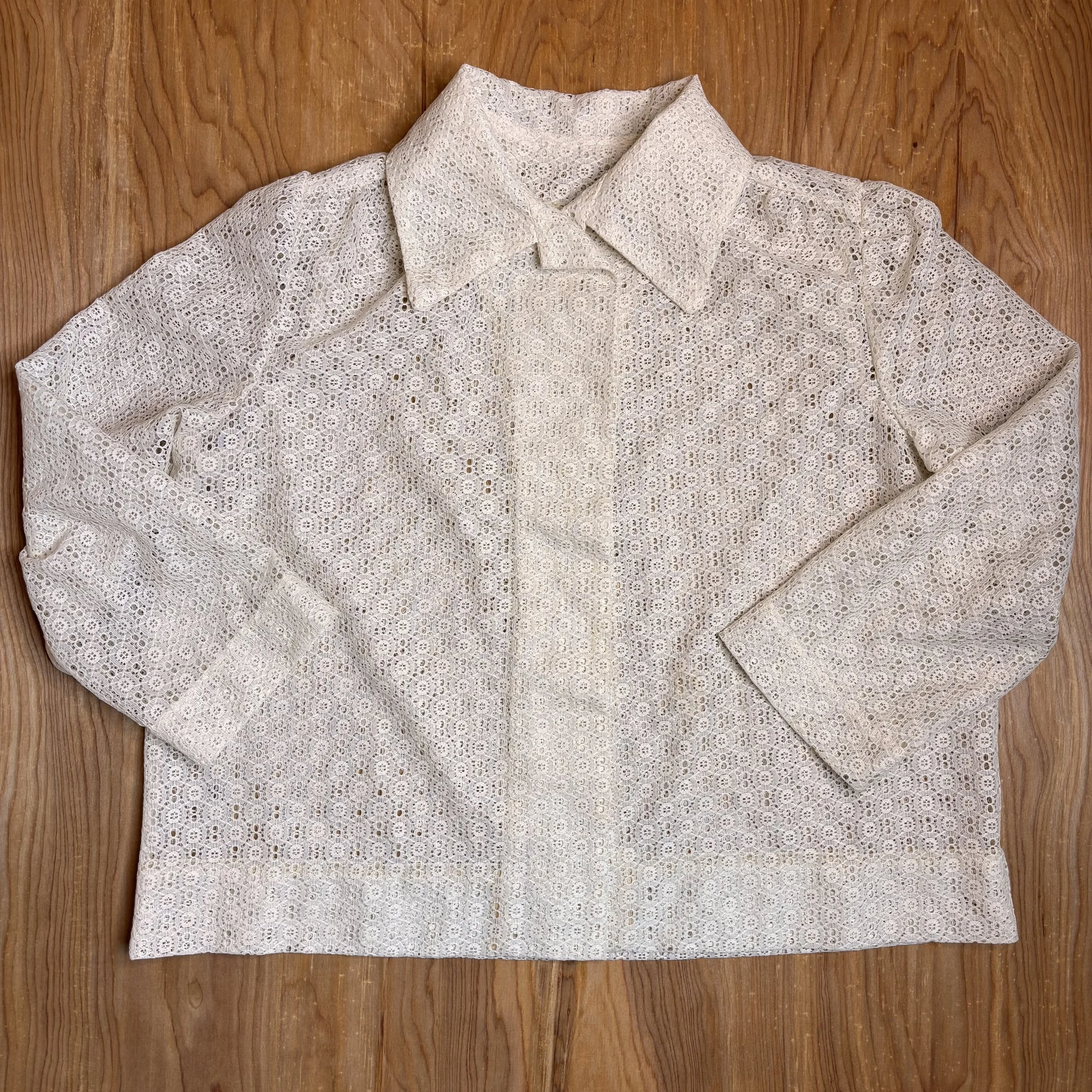 Full view of vintage 1970s cream lace button-up shirt laid flat on wood background.