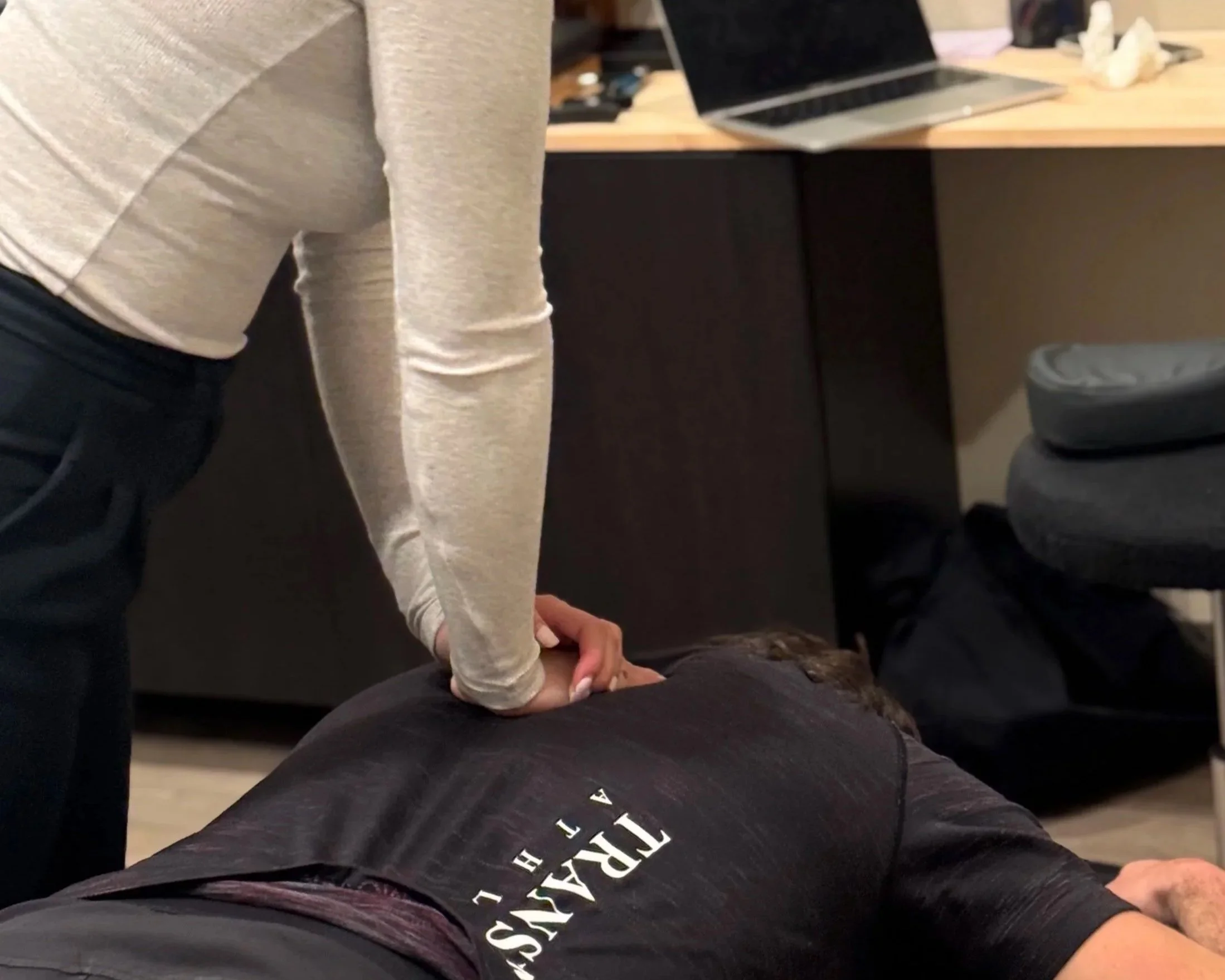 A person administering a shoulder vaccine to a young woman in a clinical setting, with the healthcare worker wearing a black watch.