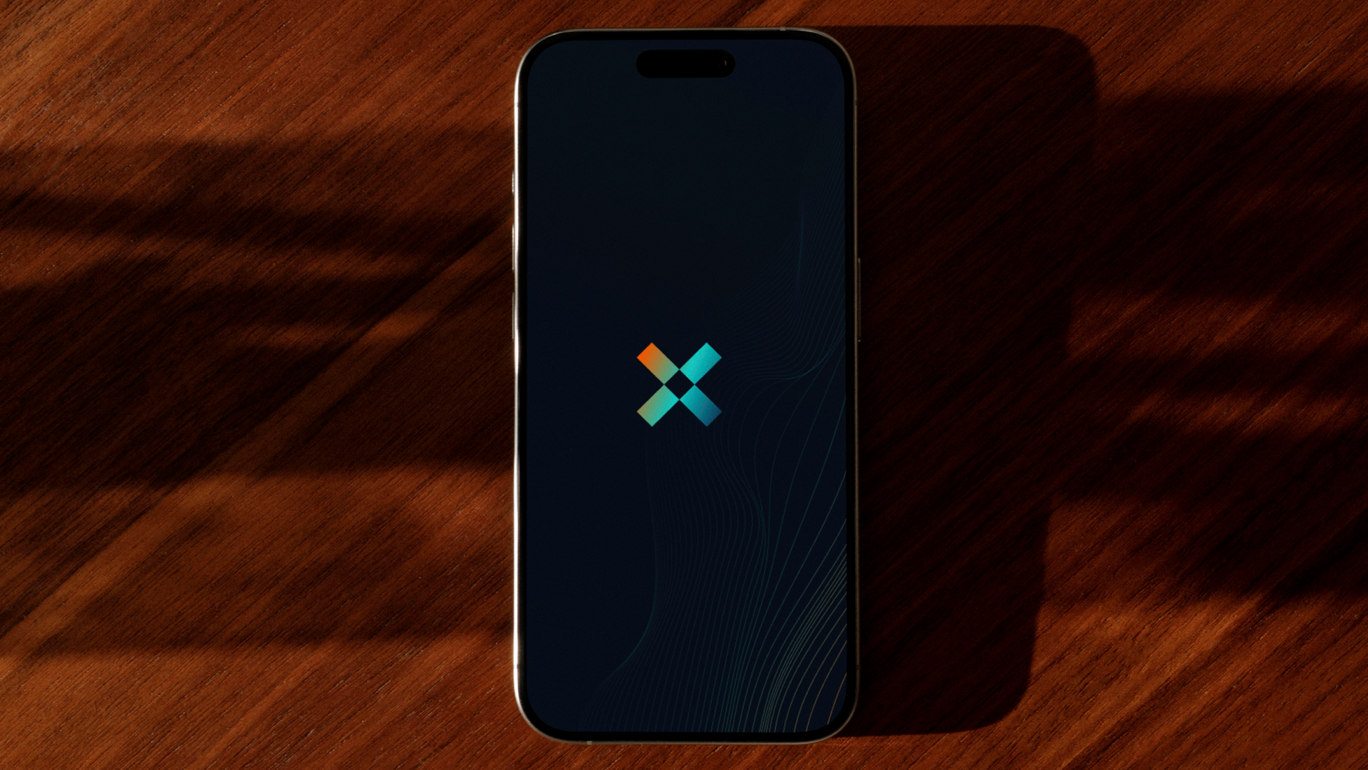 A smartphone with a dark screen displaying a colorful 'X' logo, placed on a wooden surface, casting a shadow to the right.