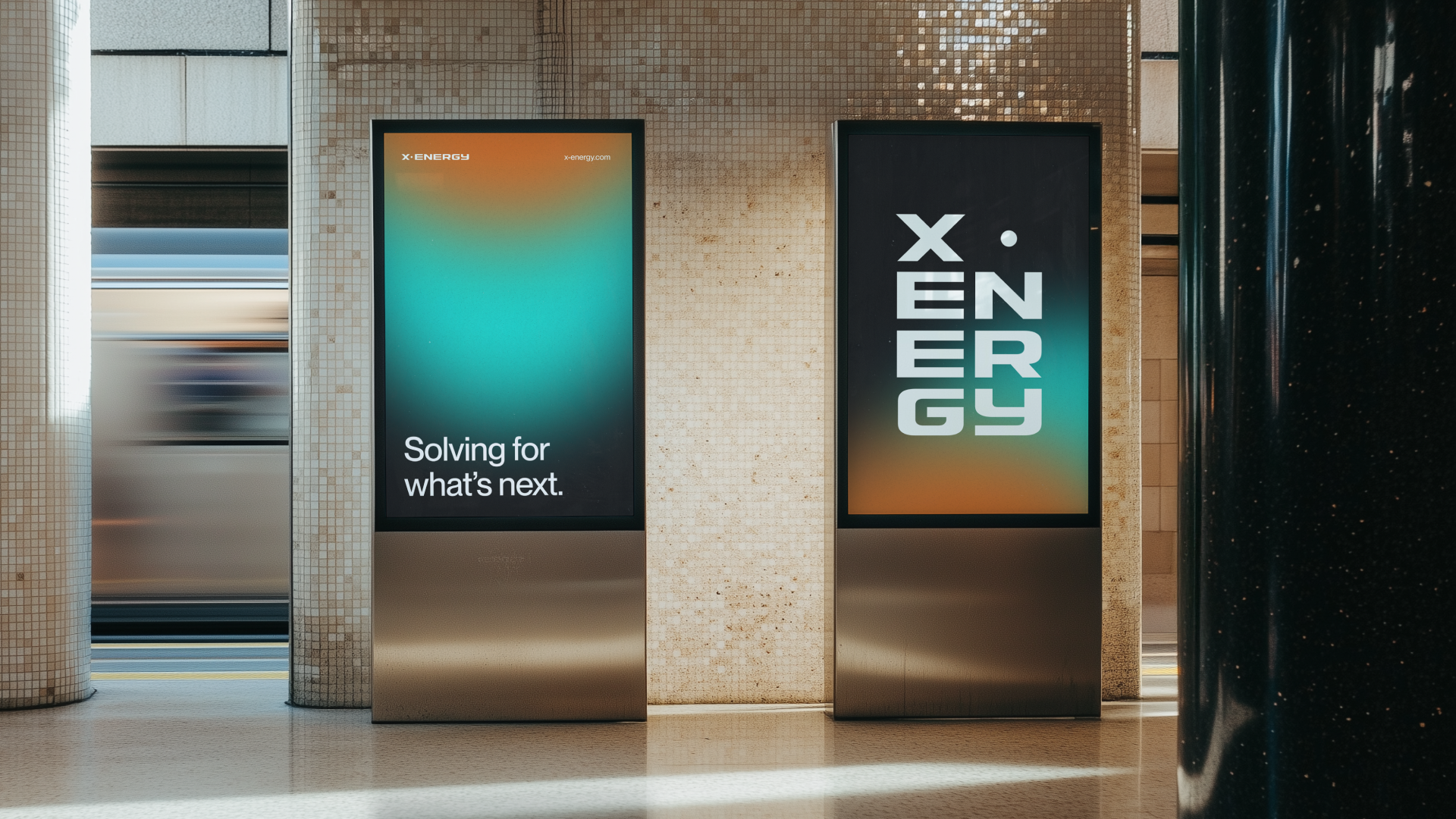 Two digital advertising screens in a train station, one displaying the message 'Solving for what's next.' and the other showing the word 'ENERGY' in bold letters with a gradient background.