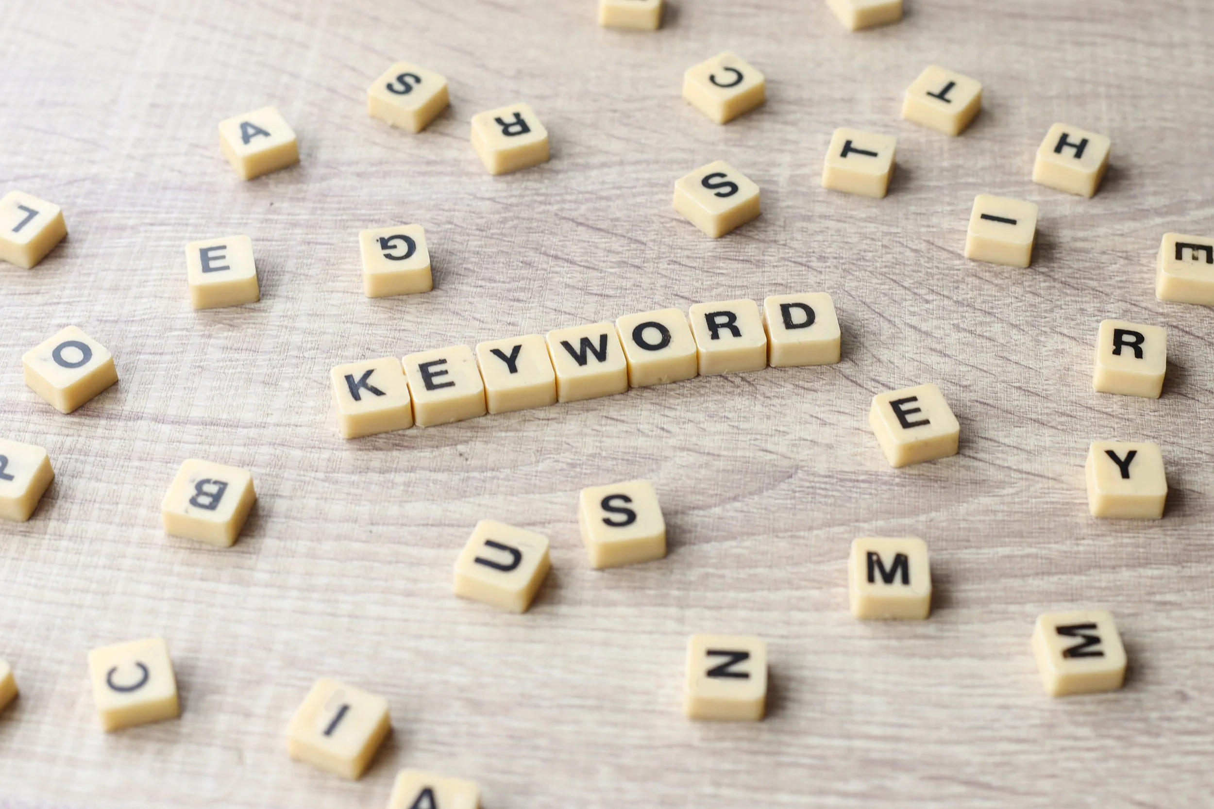 Scrabble-style letter tiles spelling out "KEYWORD" surrounded by loose scattered letter tiles on a wooden surface.