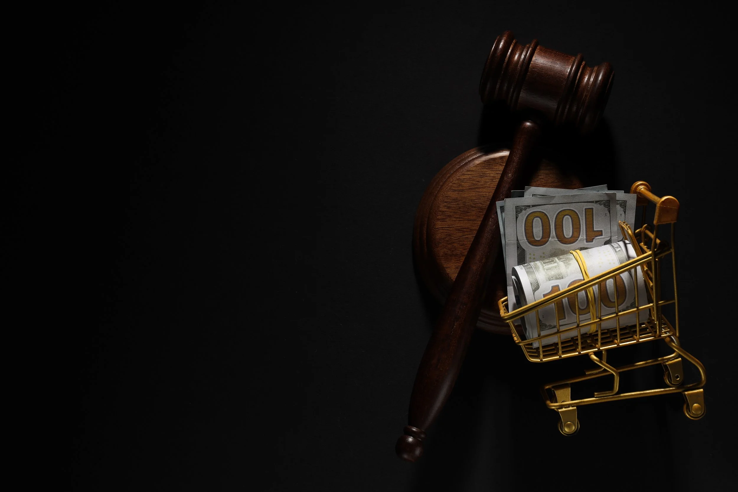 Auction gavel beside a shopping cart filled with cash, representing Amazon search as a bidding marketplace for attention