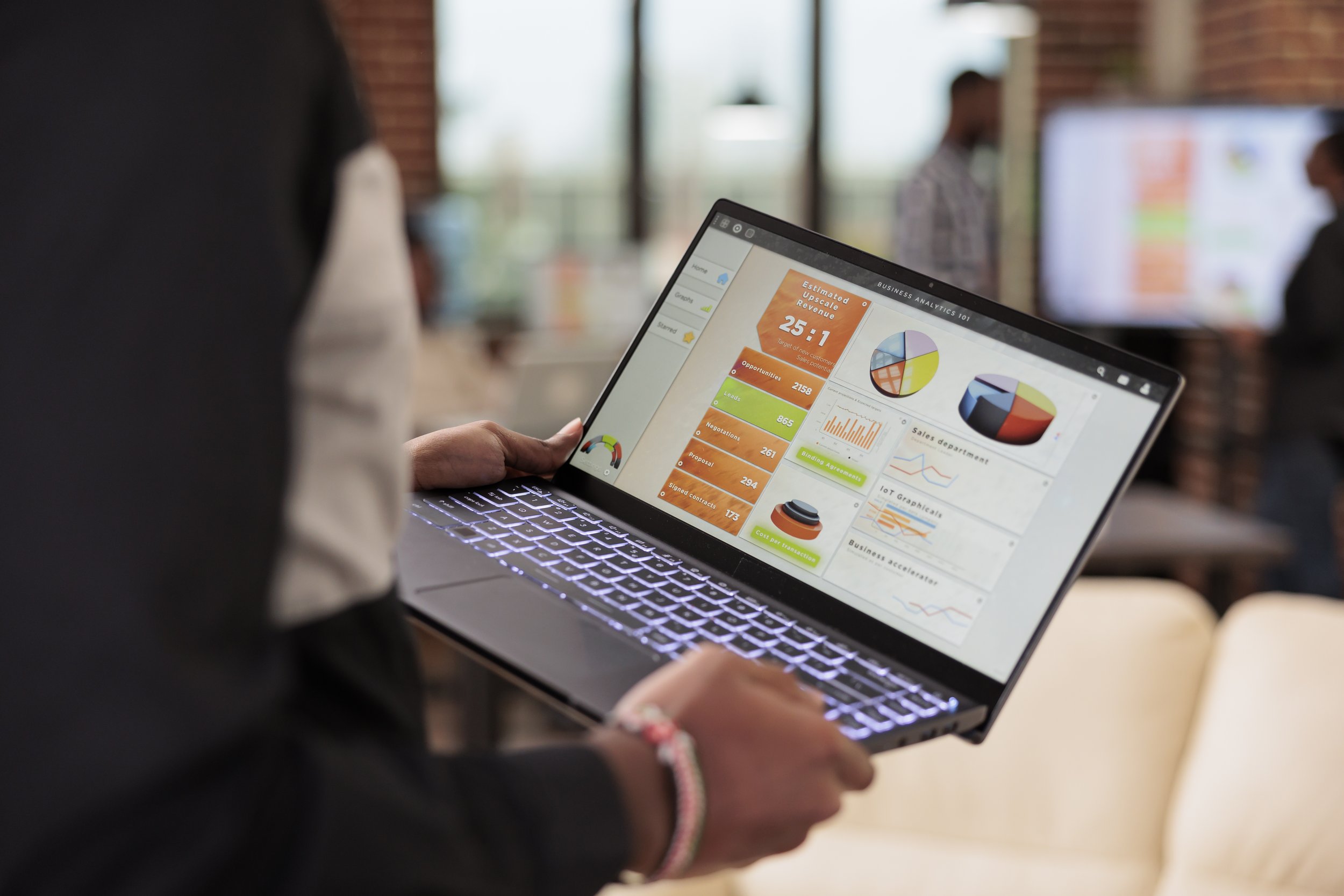 Person holding an open laptop displaying a sales and revenue analytics dashboard with charts and pipeline metrics.