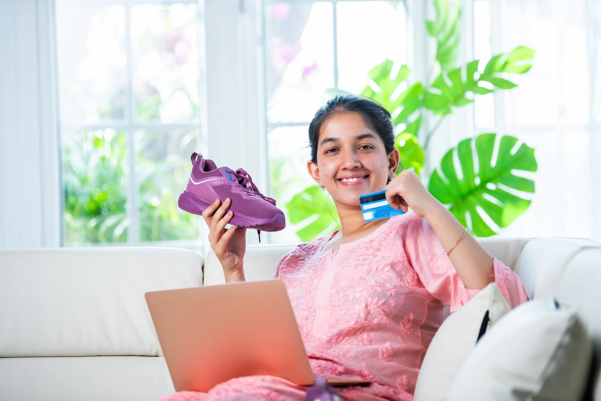 Happy customer holding a new shoe purchase and a credit card while shopping online on her laptop
