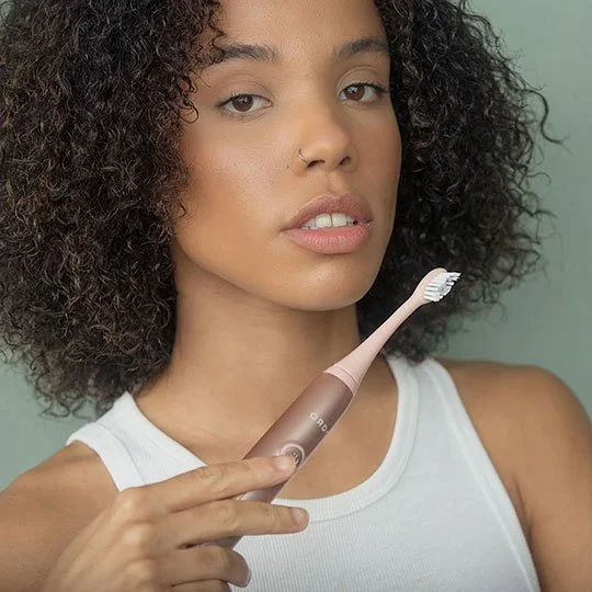 Woman using a rose gold sonic toothbrush