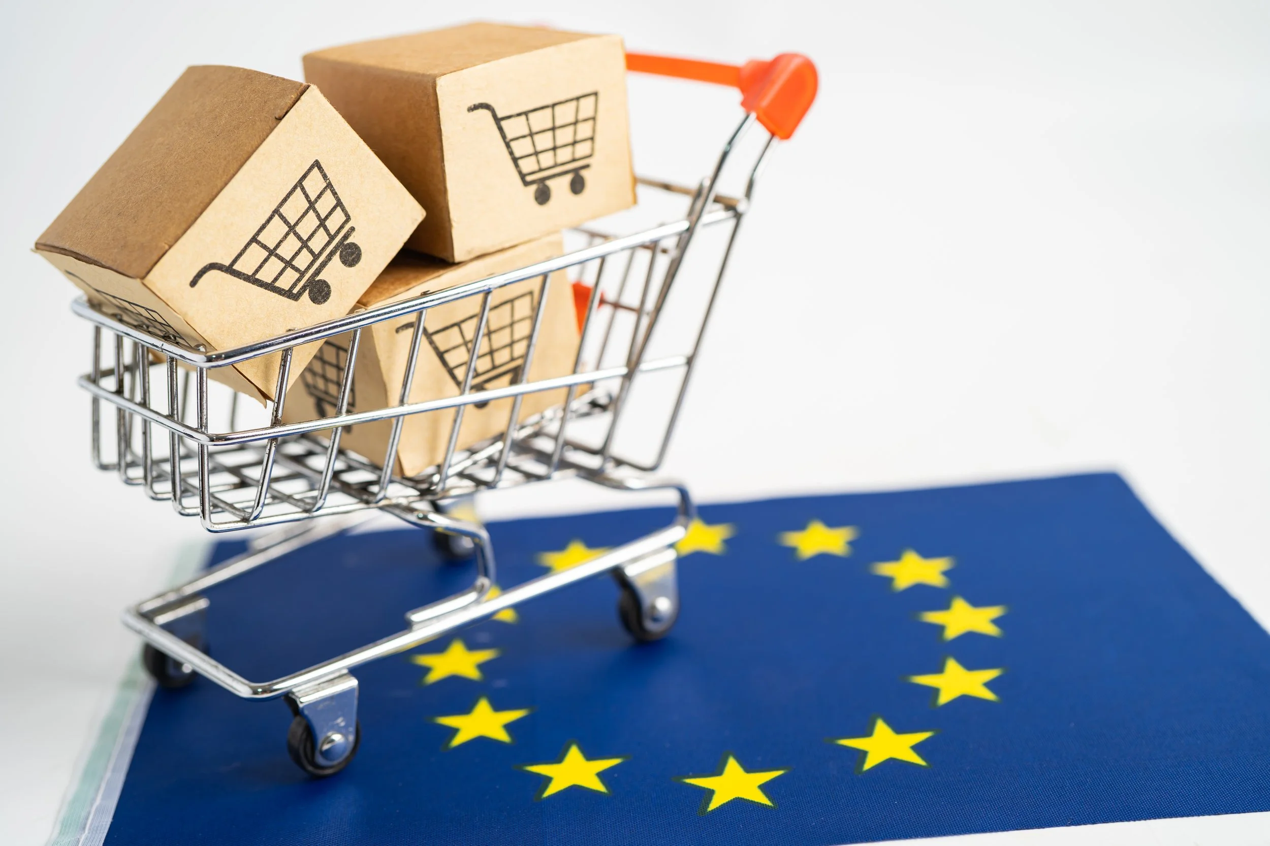 Miniature shopping cart with e-commerce boxes standing on an EU flag, symbolising cross-border selling into the EU market