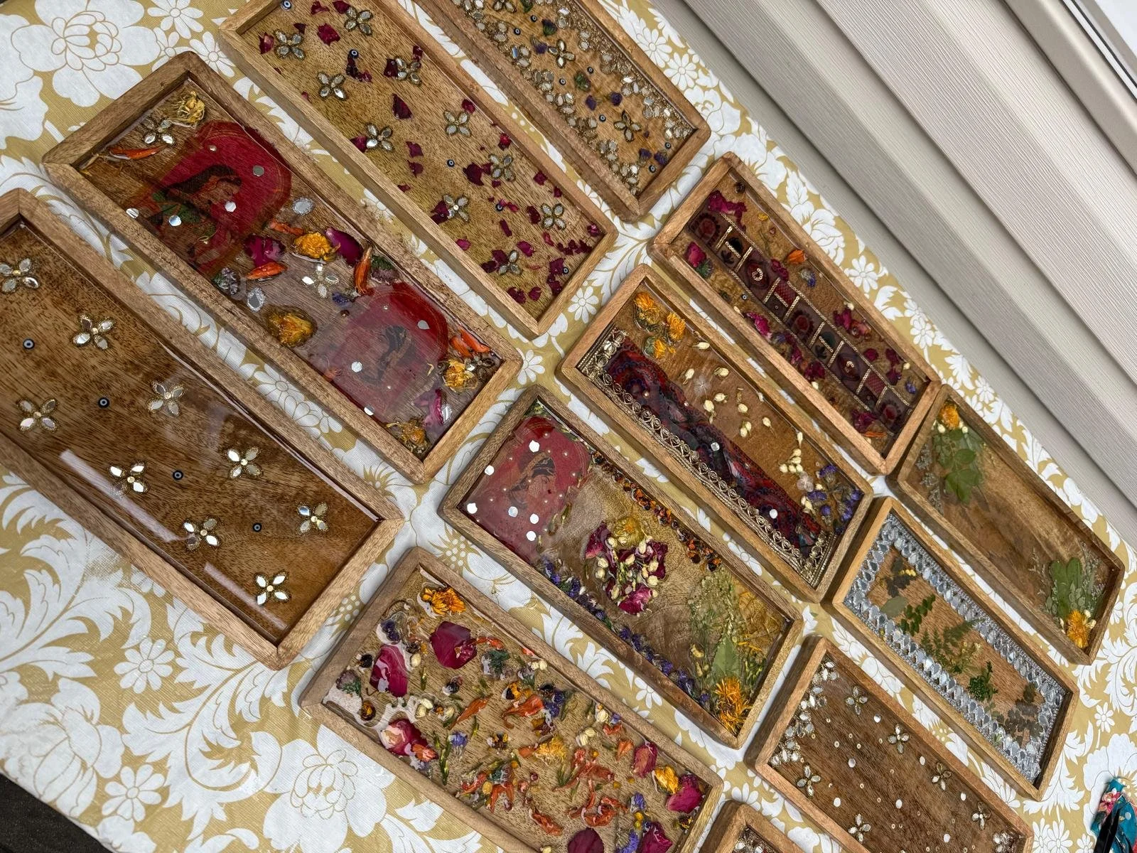 Display of wooden shadow boxes filled with dried flowers, jewelry, and decorative items on a patterned tablecloth.