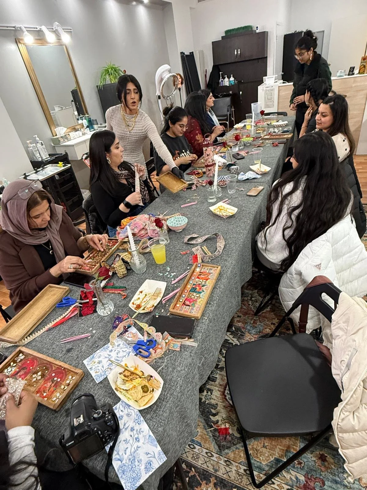 Group of women participating in a craft workshop at a long table with craft supplies, decorations, and snacks.
