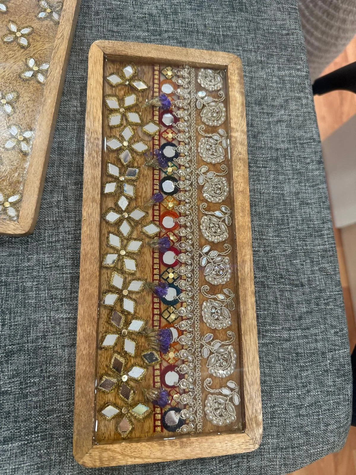 A wooden tray with various pieces of jewelry including earrings and decorative embellishments, displayed on a gray fabric surface.