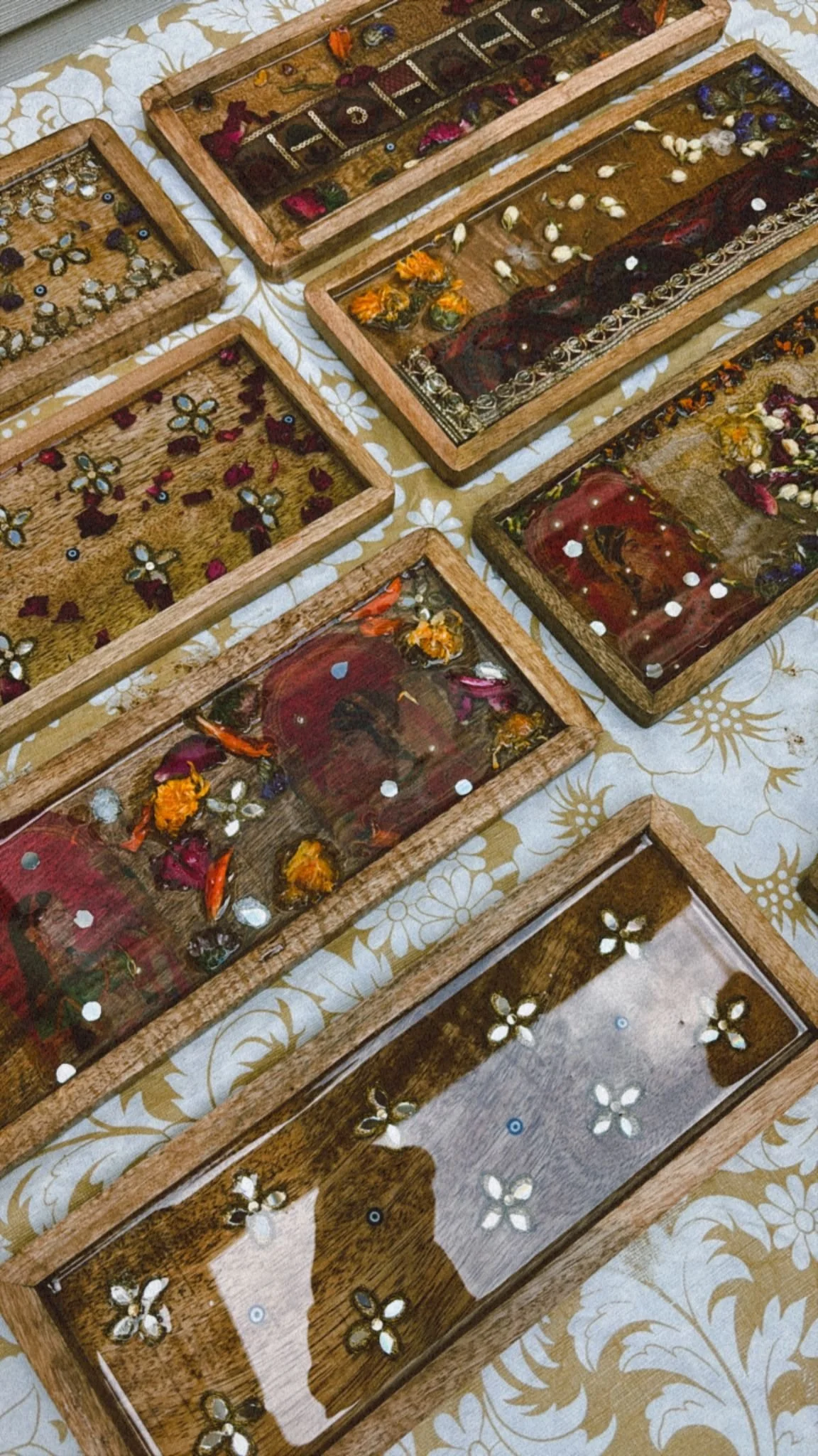 Multiple wooden shadow boxes containing jewelry and decorative items, placed on a table with a floral tablecloth.