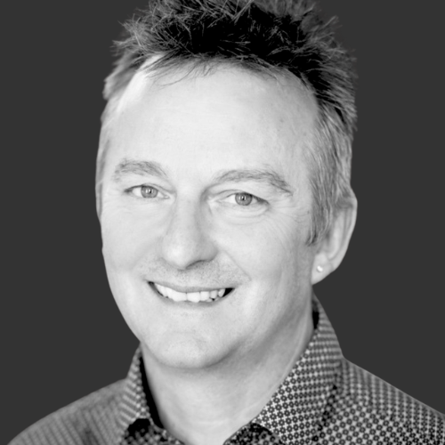 Black and white portrait of a man with spikey hair smiling at the camera.