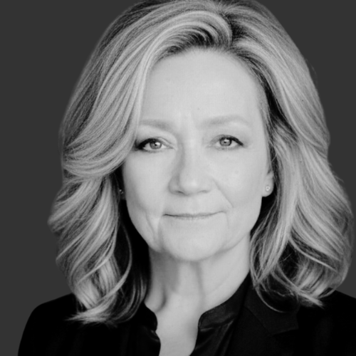 Black and white portrait of a woman with glasses, shoulder-length hair, and a slight smile, looking upward.
