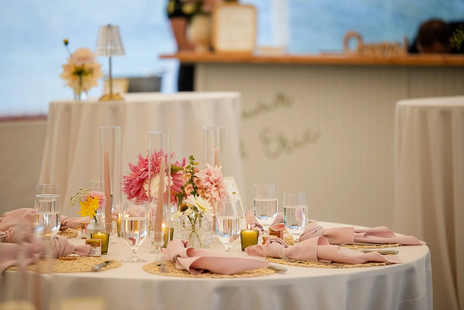 A round banquet table decorated with pink flowers, pink napkins, and glassware at a wedding reception.