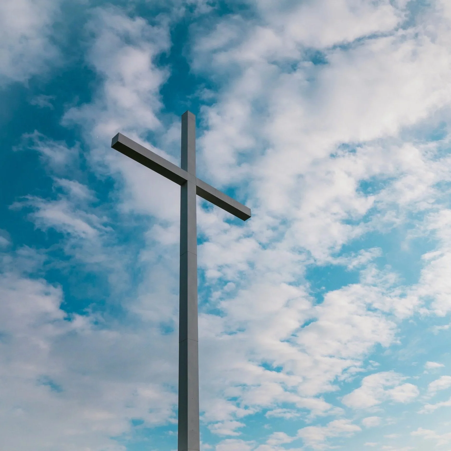 A large white cross structure set against a sky filled with blue and white clouds.