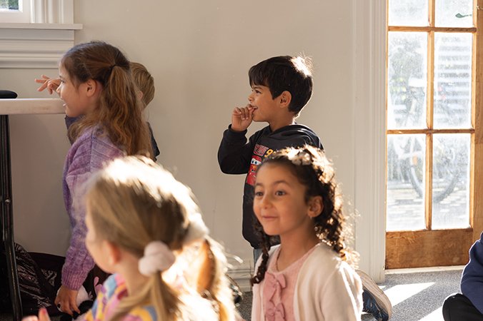 Children smiling and engaging in an indoor activity near a door with sunlight streaming in.