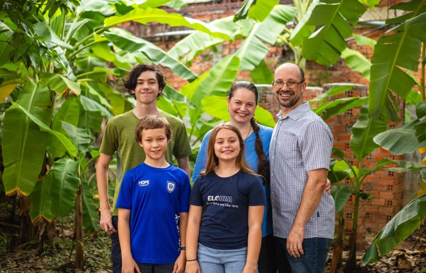 A family of six standing in a lush banana plant garden, smiling for the camera.